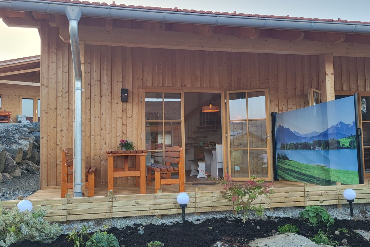 Una cabaña de madera con un porche cubierto, un comedor y un ventanal con vistas panorámicas.