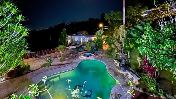 Vista nocturna d'una zona de piscina amb una casa al fons.