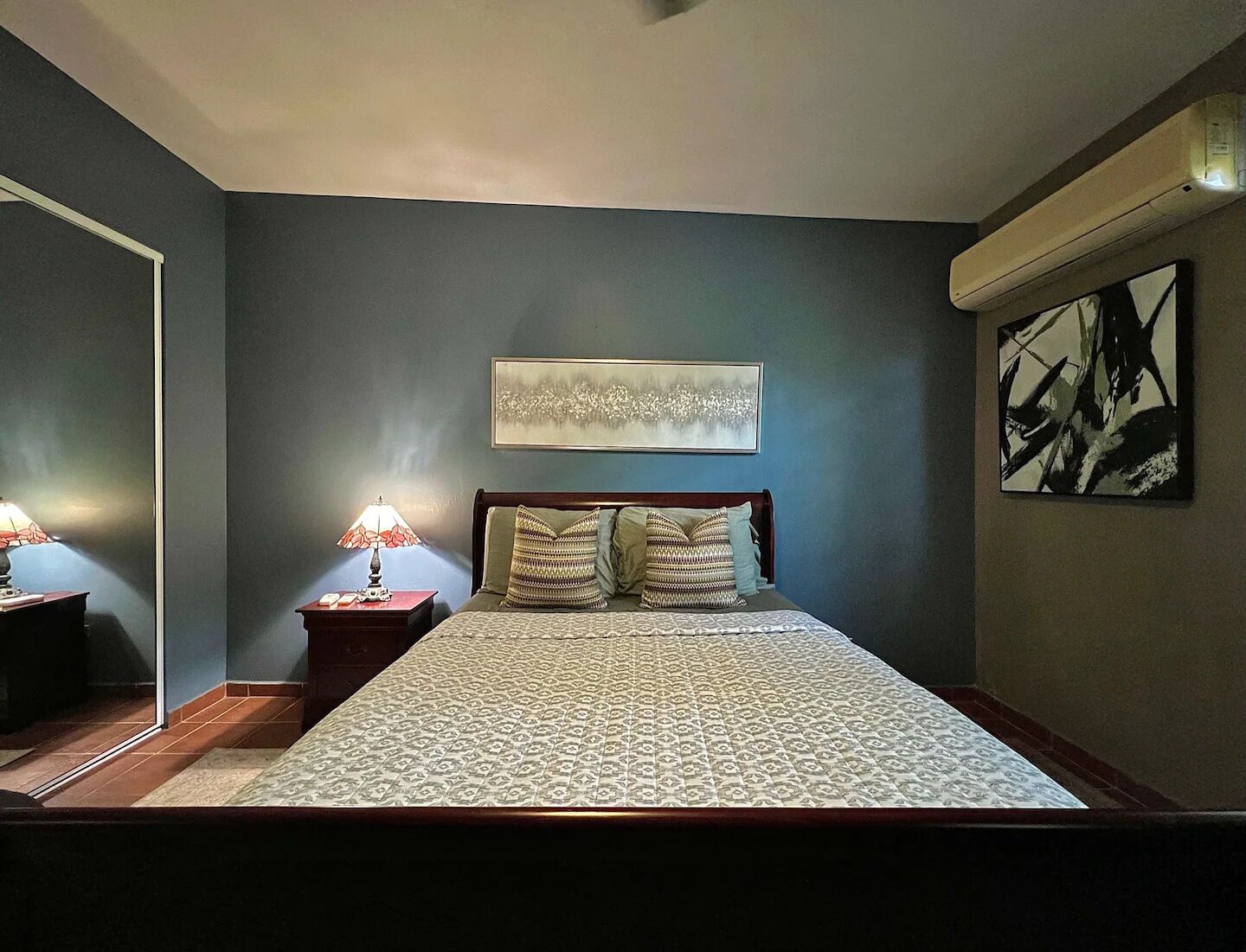 A bedroom with a bed, two bedside tables, a nightstand, a wall-mounted artwork, and a ceiling fan.