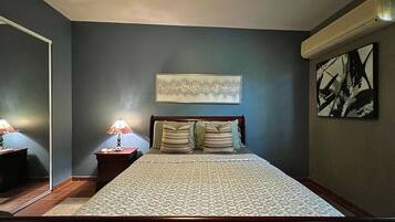 A bedroom with a bed, two bedside tables, a nightstand, a wall-mounted artwork, and a ceiling fan.