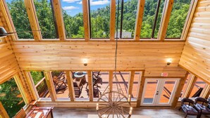 A wooden cabin with a large balcony, a rustic wooden wheel hanging from the ceiling, and a view of a forested area.
