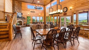 A spacious wooden cabin with a dining area, fireplace, and large windows offering scenic views.