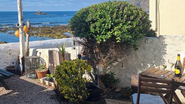 Une terrasse avec une table et des chaises, un petit jardin et une vue sur la mer.