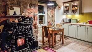 Une cuisine rustique avec une cheminée en pierre, une table à manger en bois et des armoires de couleur claire.
