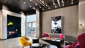 A modern lounge area with a sofa, armchairs, a coffee table, and a large abstract painting on the wall. - Aloft by Marriott Lawrenceville Sugarloaf (Lawrenceville)