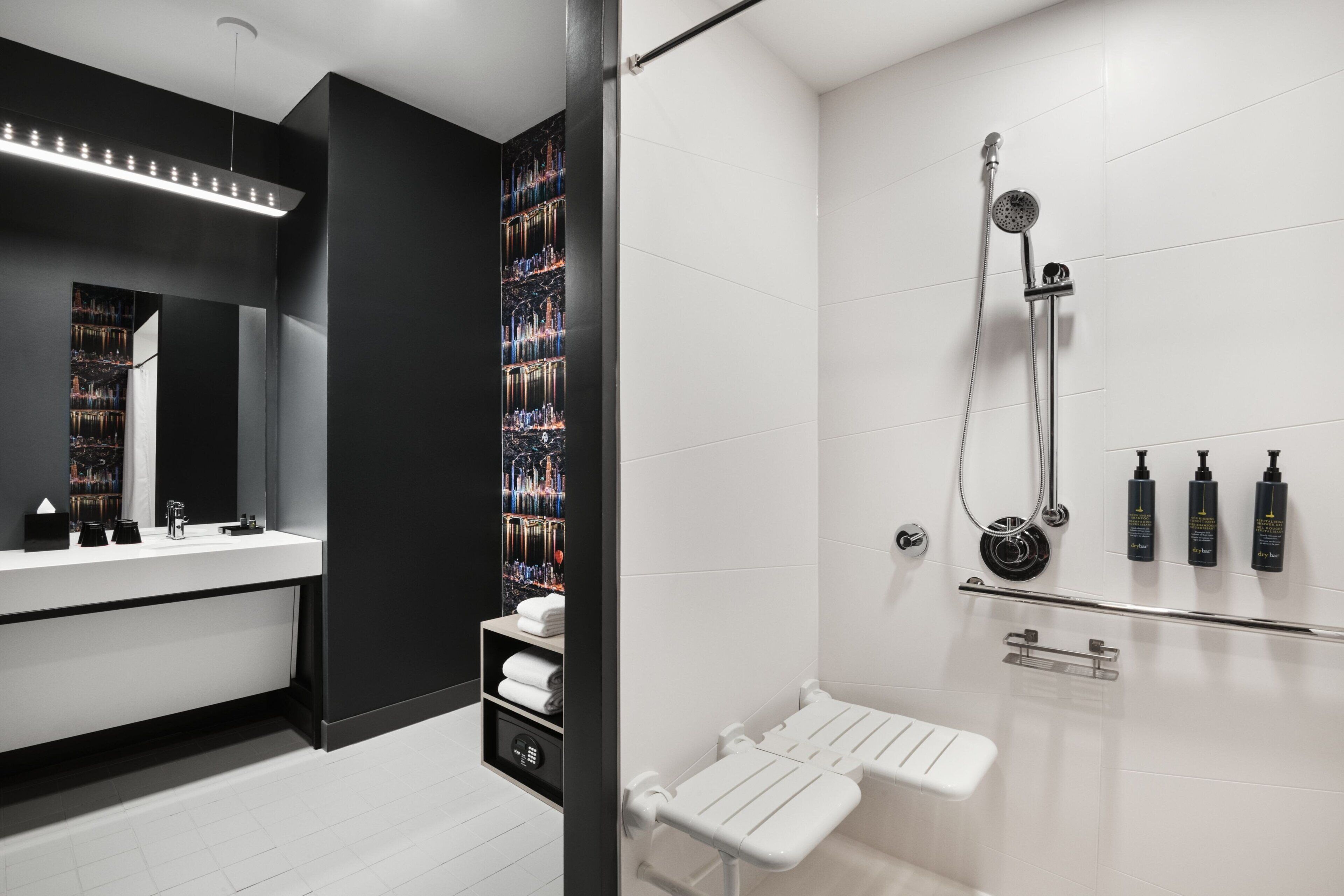 Une salle de bain moderne avec un grand miroir, un lavabo blanc, une douche équipée d’un pommeau de douche à main et un porte-serviettes.