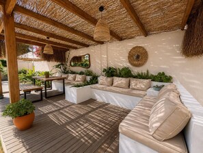 Un espacio al aire libre con terraza de madera, asientos acolchados y techo de paja.
