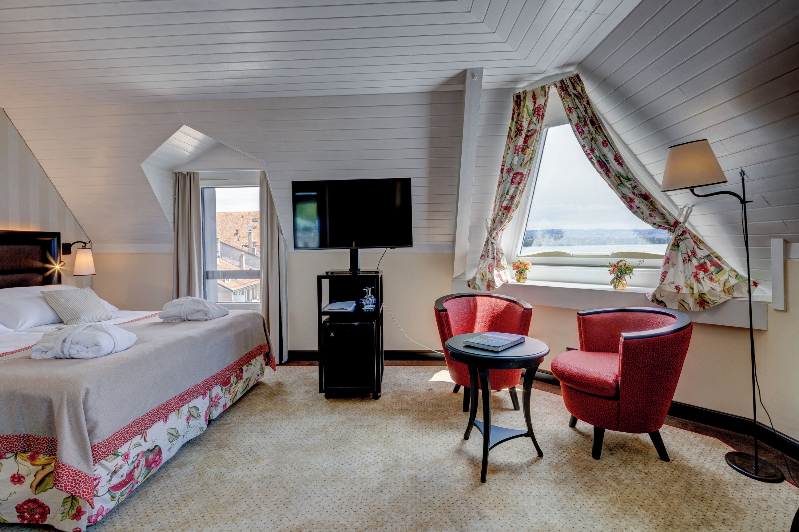 Habitación de hotel con cama, escritorio con computadora, dos sillas, televisor y ventana con cortinas.