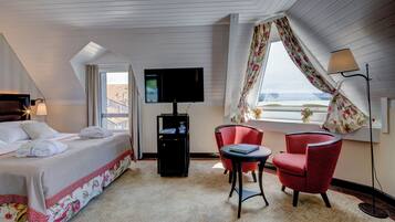 Habitación de hotel con cama, escritorio con computadora, dos sillas, televisor y ventana con cortinas.
