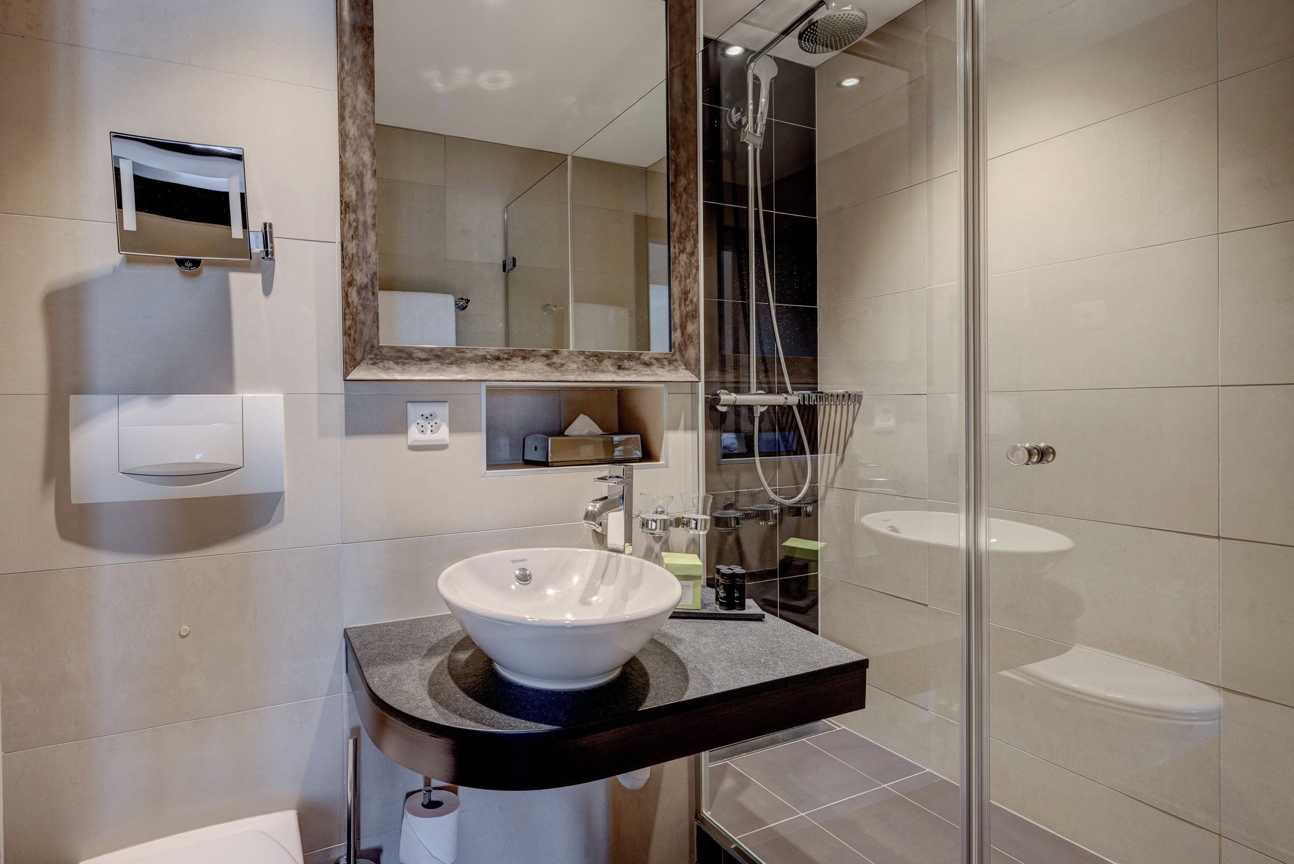 A modern bathroom with a large mirror, a vessel sink, a shower, and a toilet.