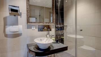 A modern bathroom with a large mirror, a vessel sink, a shower, and a toilet.