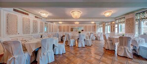 Un salón de banquetes con varias mesas redondas, manteles blancos y sillas con fundas blancas.