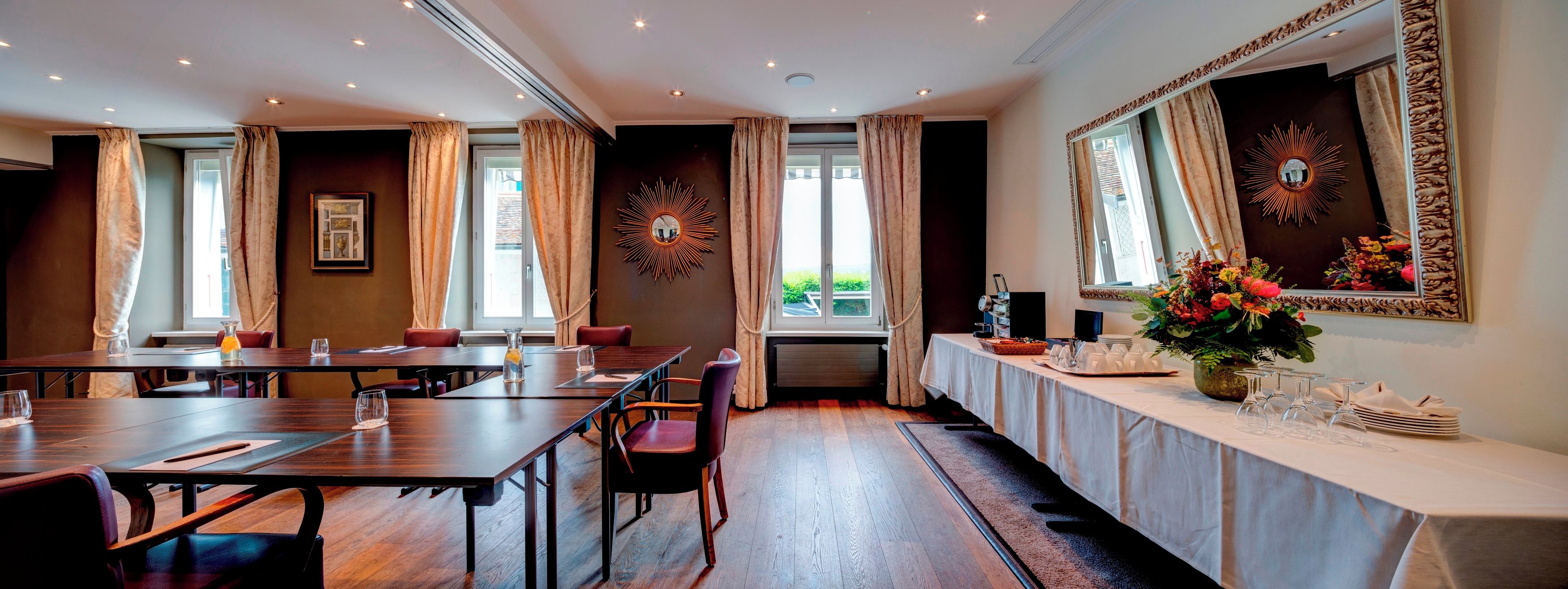 A conference room with a long table, chairs, and a buffet table with plates and glasses.