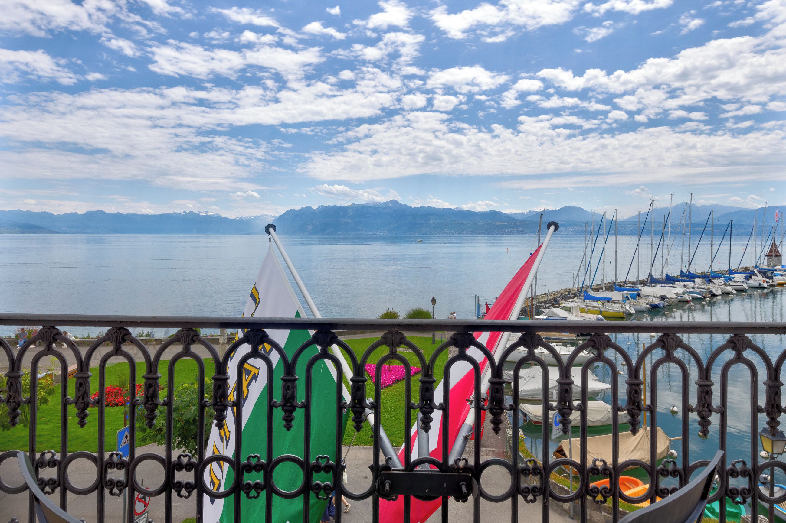 Una marina con barcos, cielo despejado y montañas al fondo.