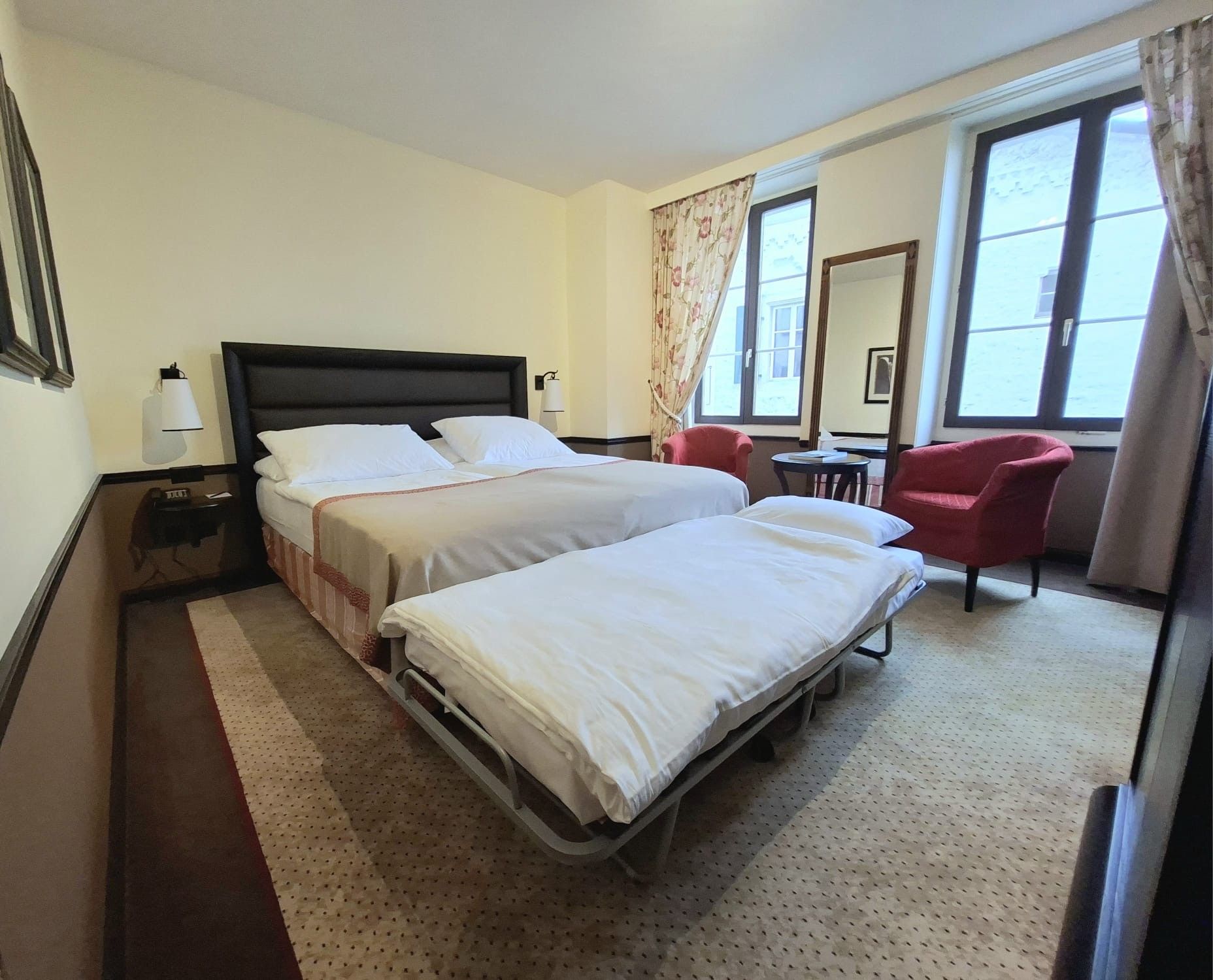 Una habitación de hotel con dos camas, un escritorio, una silla y ventanas amplias.
