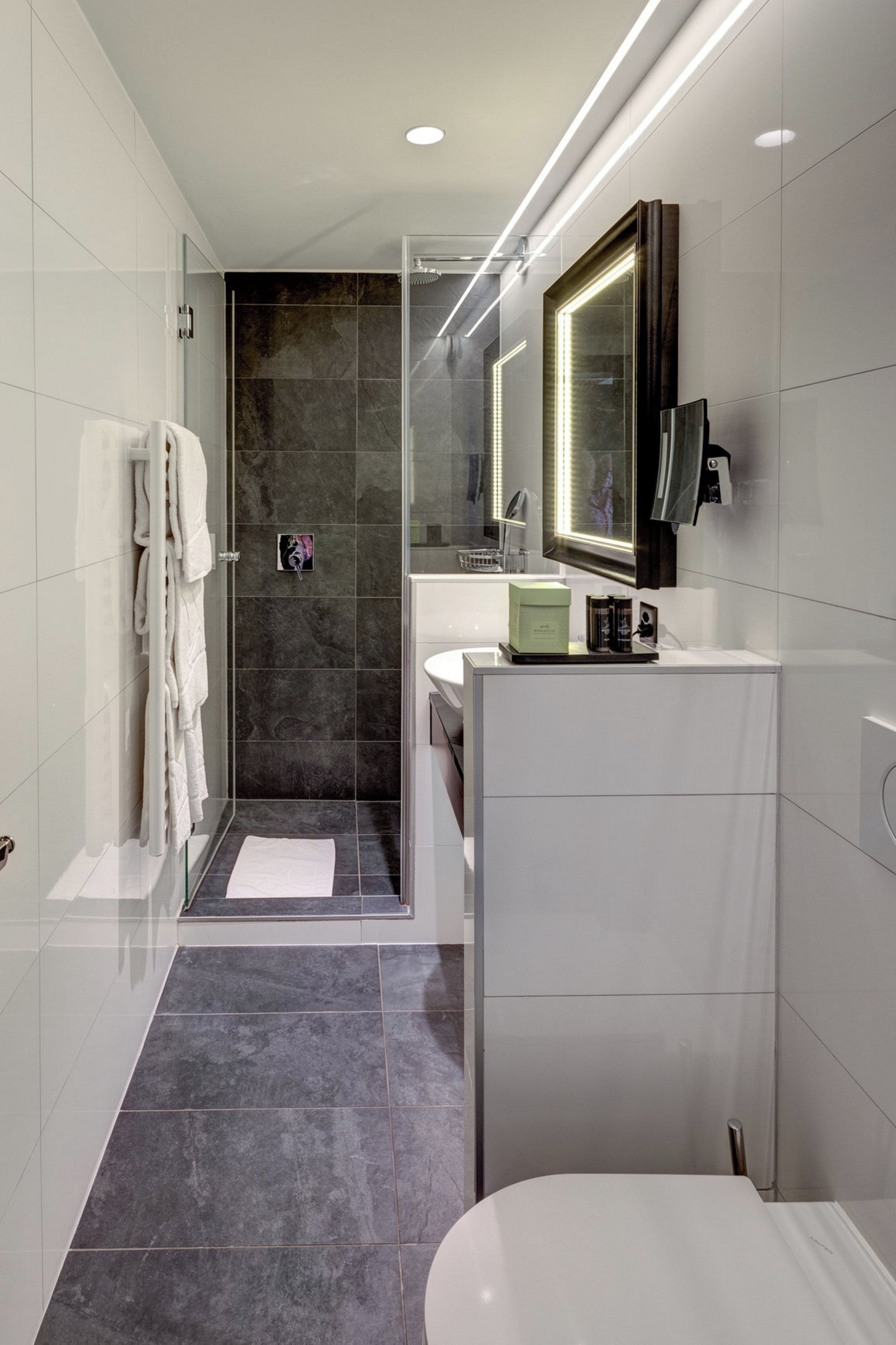 Un baño moderno con ducha envuelta en vidrio, tocador con espejo y retrete.