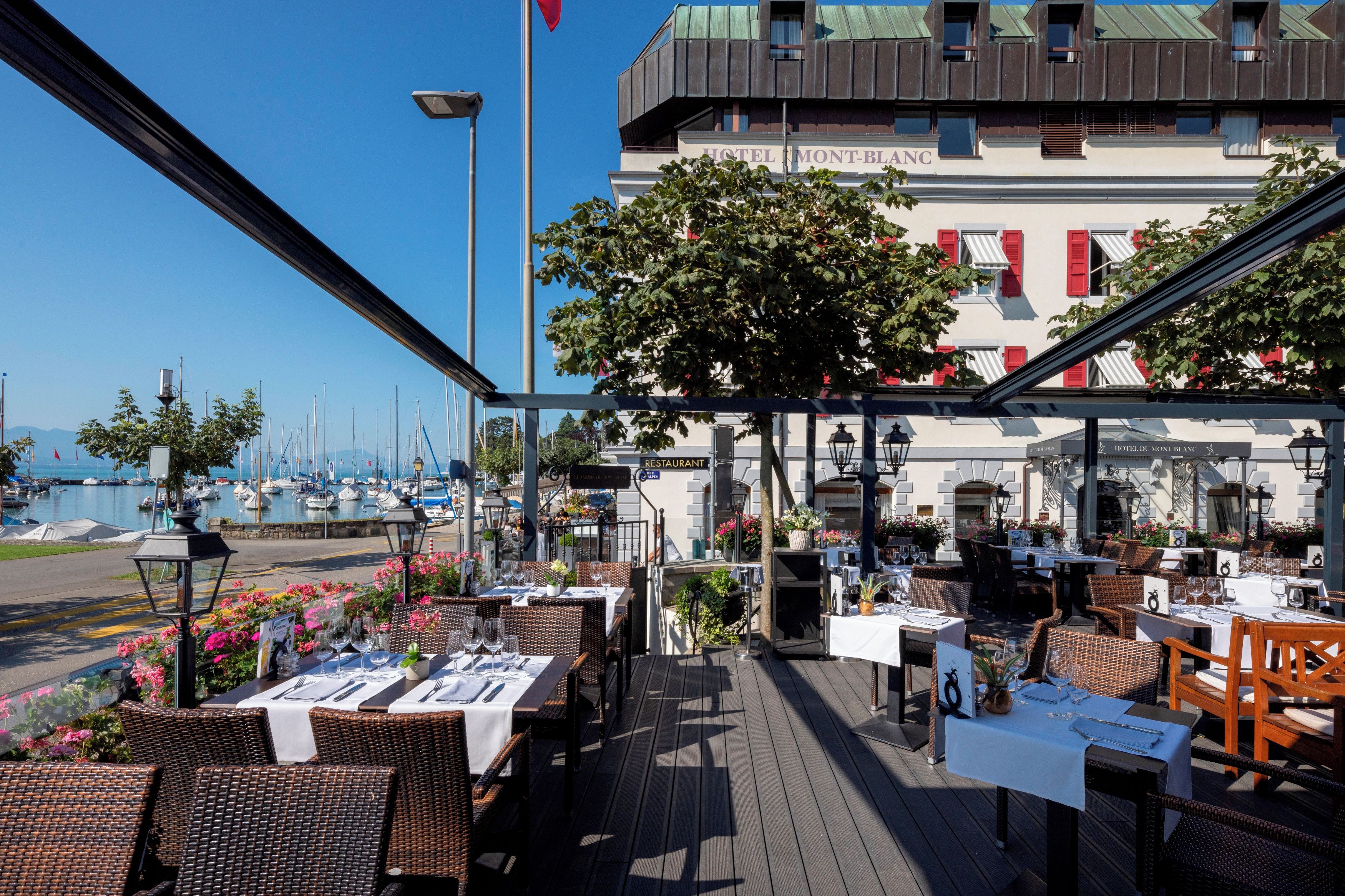 Un área de comedor al aire libre con mesas y sillas, con vista a un puerto deportivo y barcos.