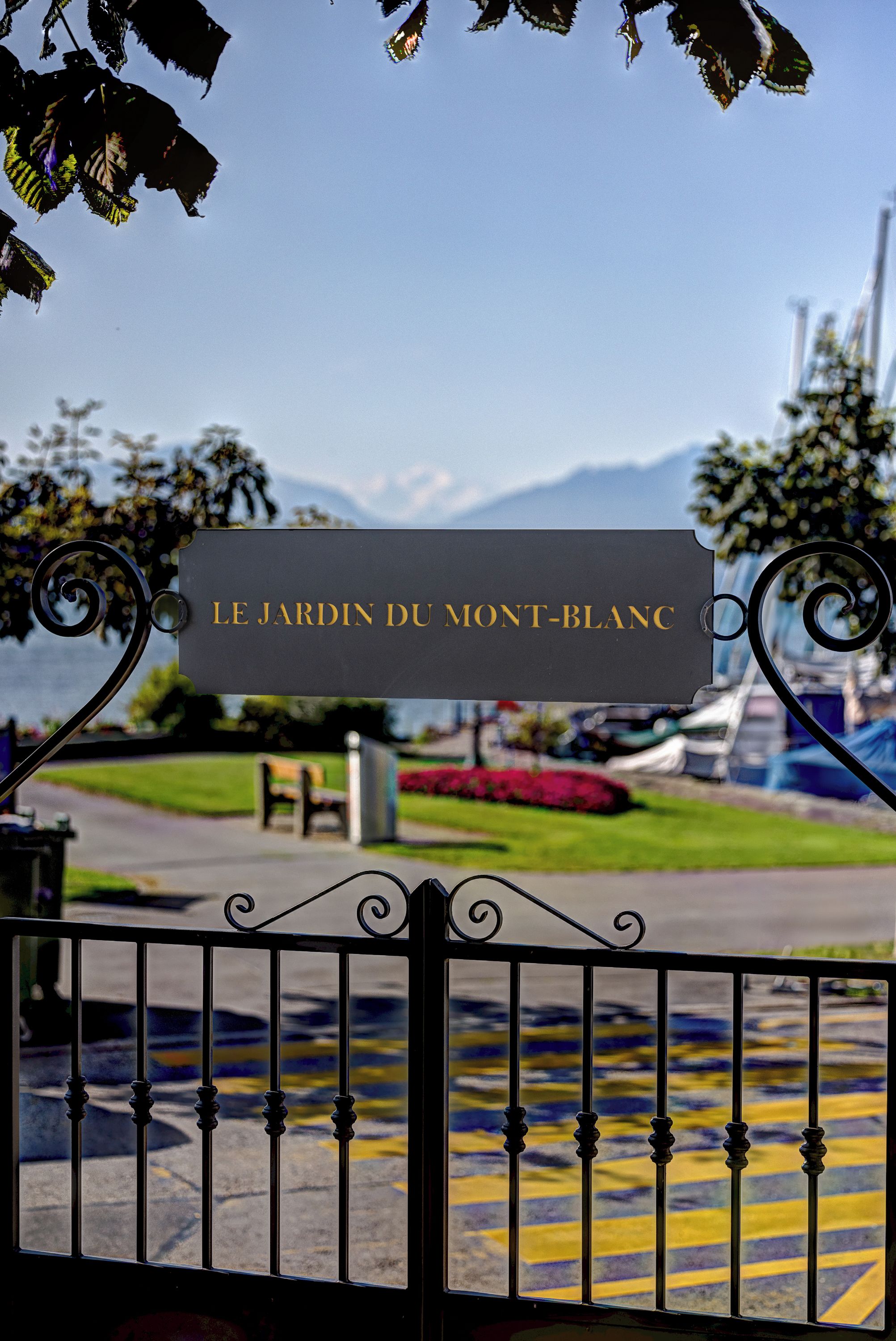 A sign with the text 'LE JARDIN DU MONT-BLANCH' indicating a location, with a view of a park and mountains in the background.