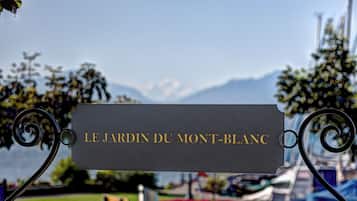 A sign with the text 'LE JARDIN DU MONT-BLANCH' indicating a location, with a view of a park and mountains in the background.