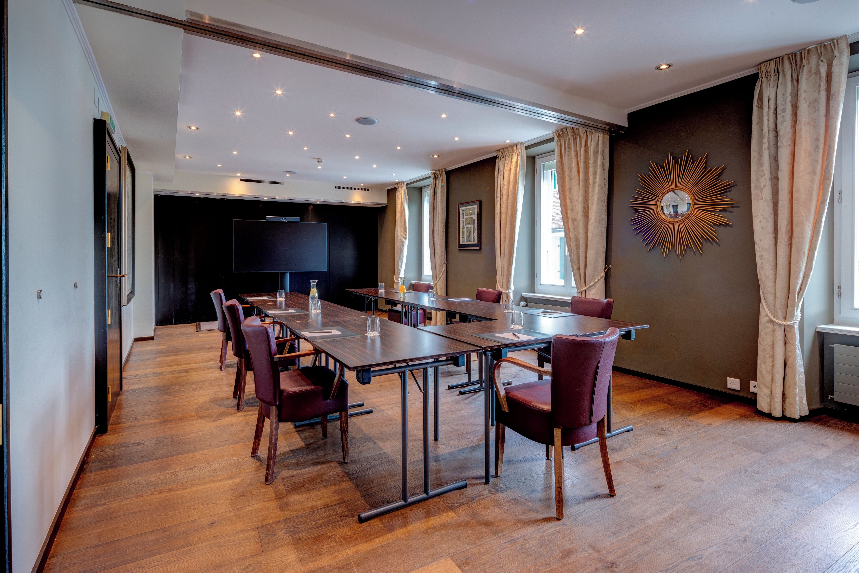 Ein Konferenzraum mit langem Tisch, Stühlen, einer großen Leinwand und einem dekorativen Wandelement.