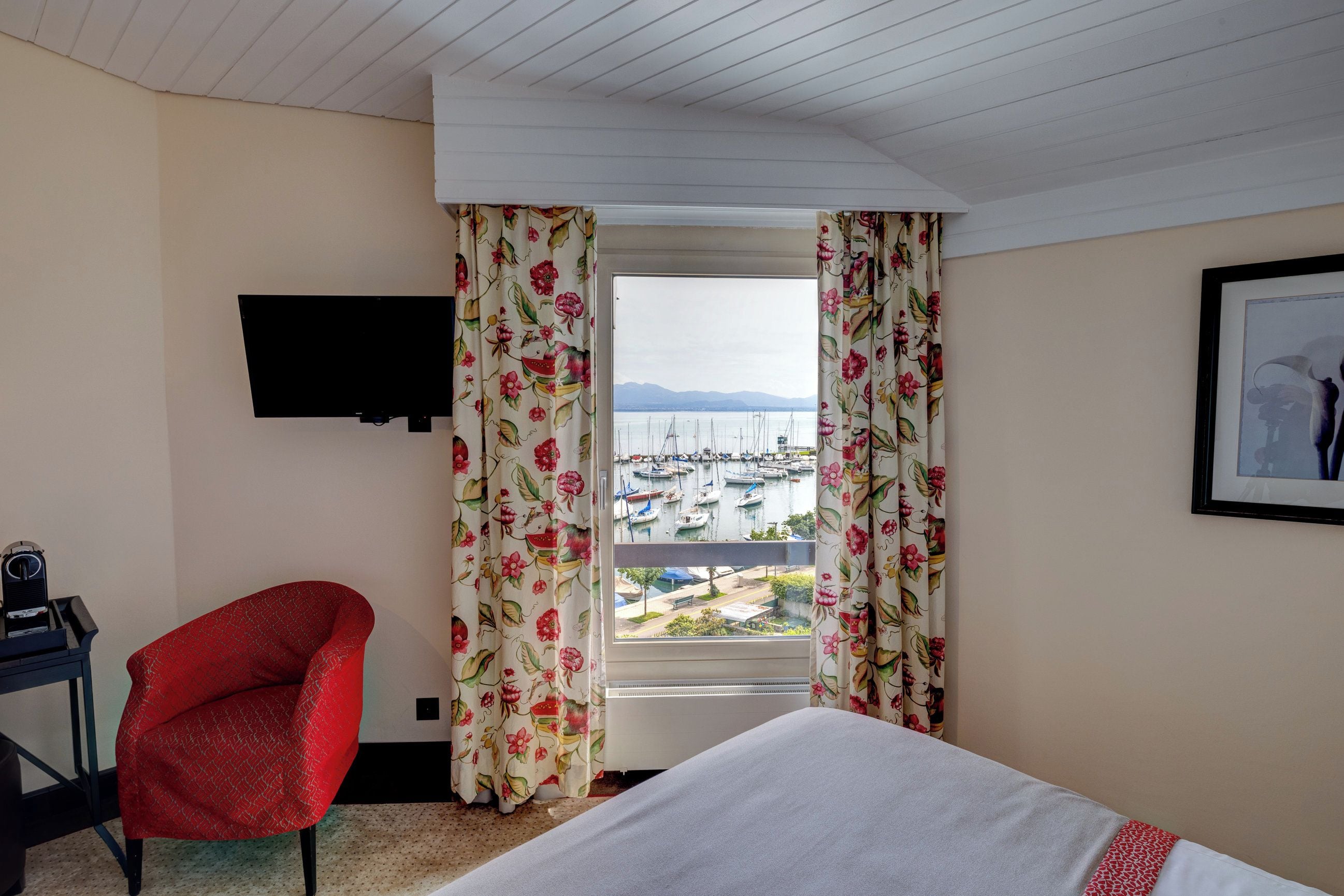 Habitación de hotel con cama, escritorio, silla, televisor y ventana con cortinas.