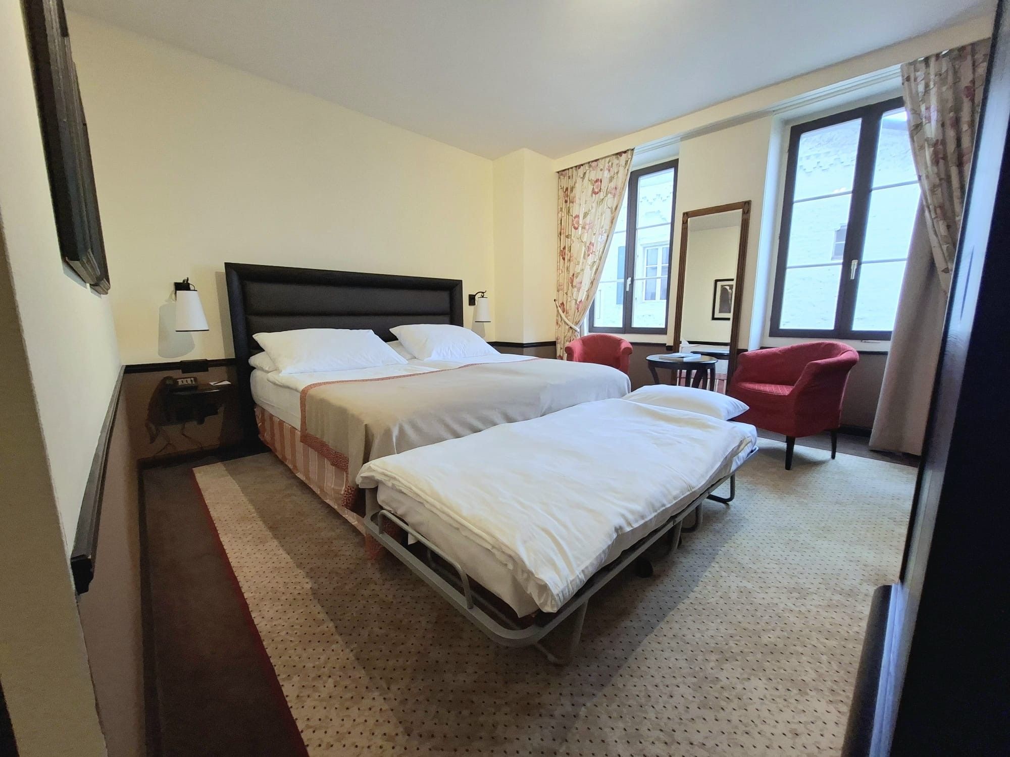 Ein Hotelzimmer mit einem Doppelbett, einem Schreibtisch, einem Stuhl und einem fenster mit Vorhängen.