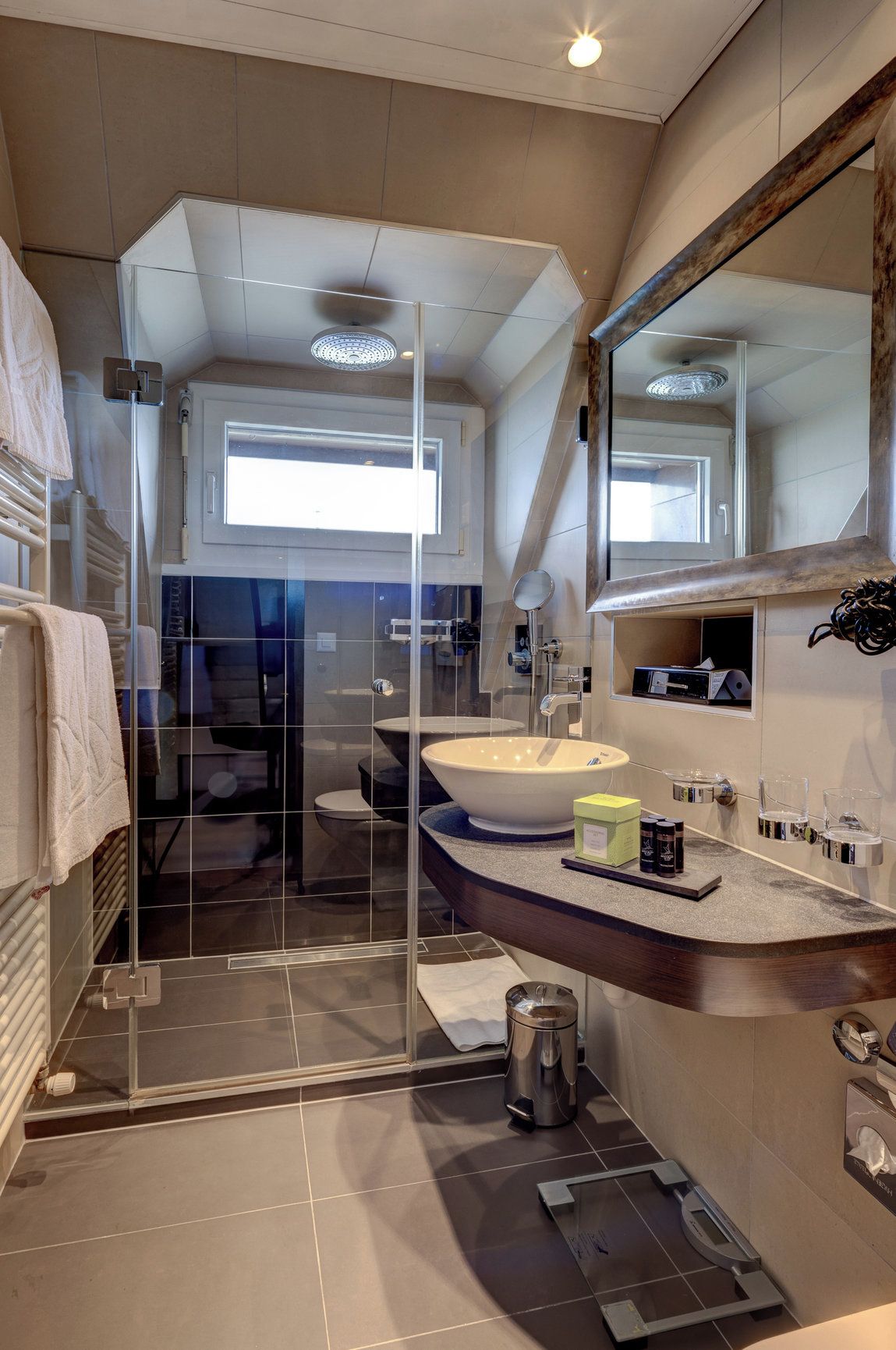 A modern bathroom with a glass shower enclosure, a large sink, and a vanity with toiletries.