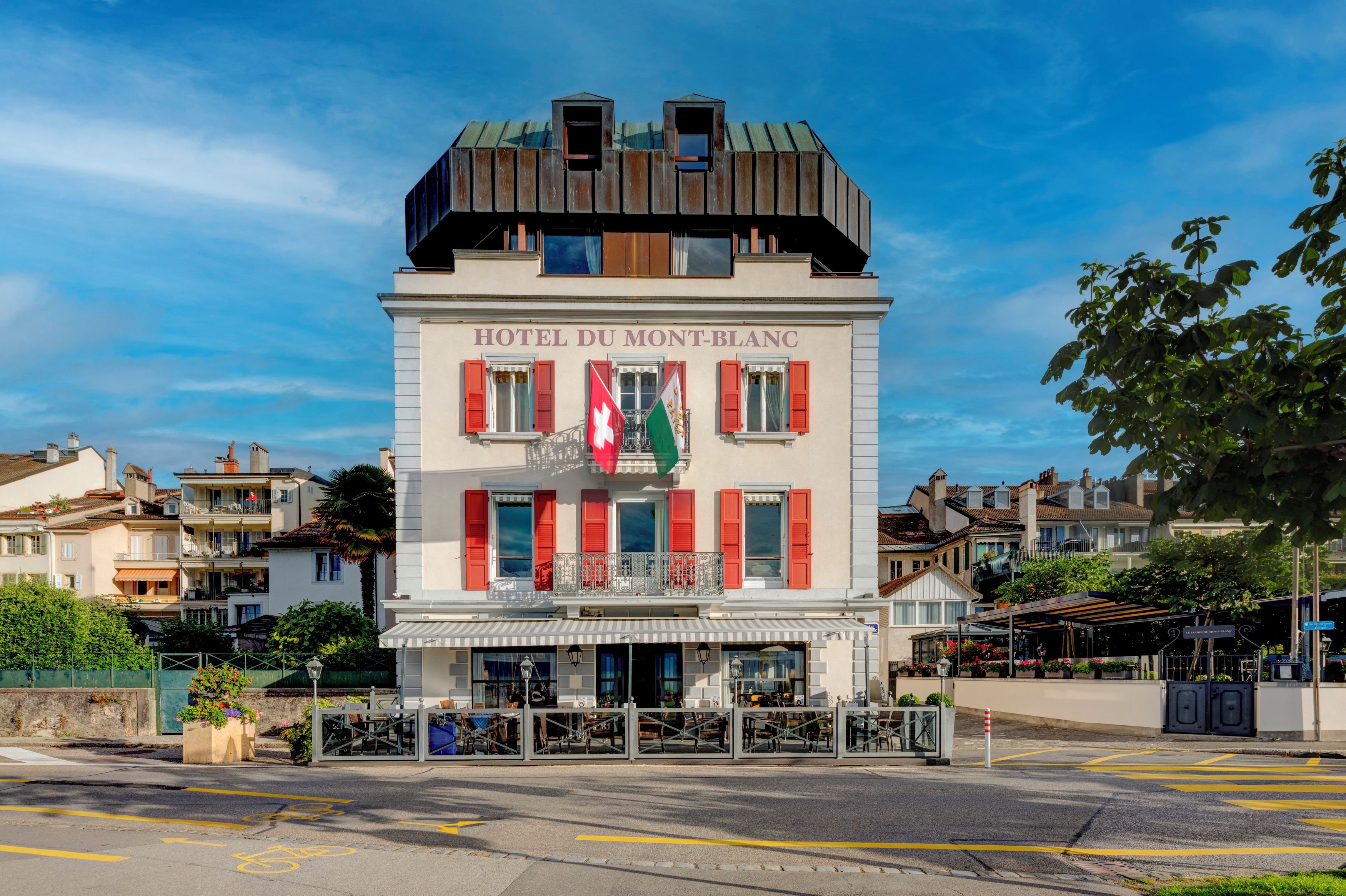 Ein Hotel namens 'HOTEL DU MONT-BLANC' mit klassischem europäischem Baustil, das einen markanten Balkon und rote Fensterläden aufweist.