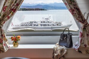 Una habitación con vistas a un lago y un bote, un florero con flores y un bolso sobre un alféizar.