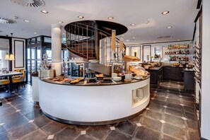 Zona de bar moderna con una isla central, una escalera en espiral y una amplia variedad de comida y bebidas.