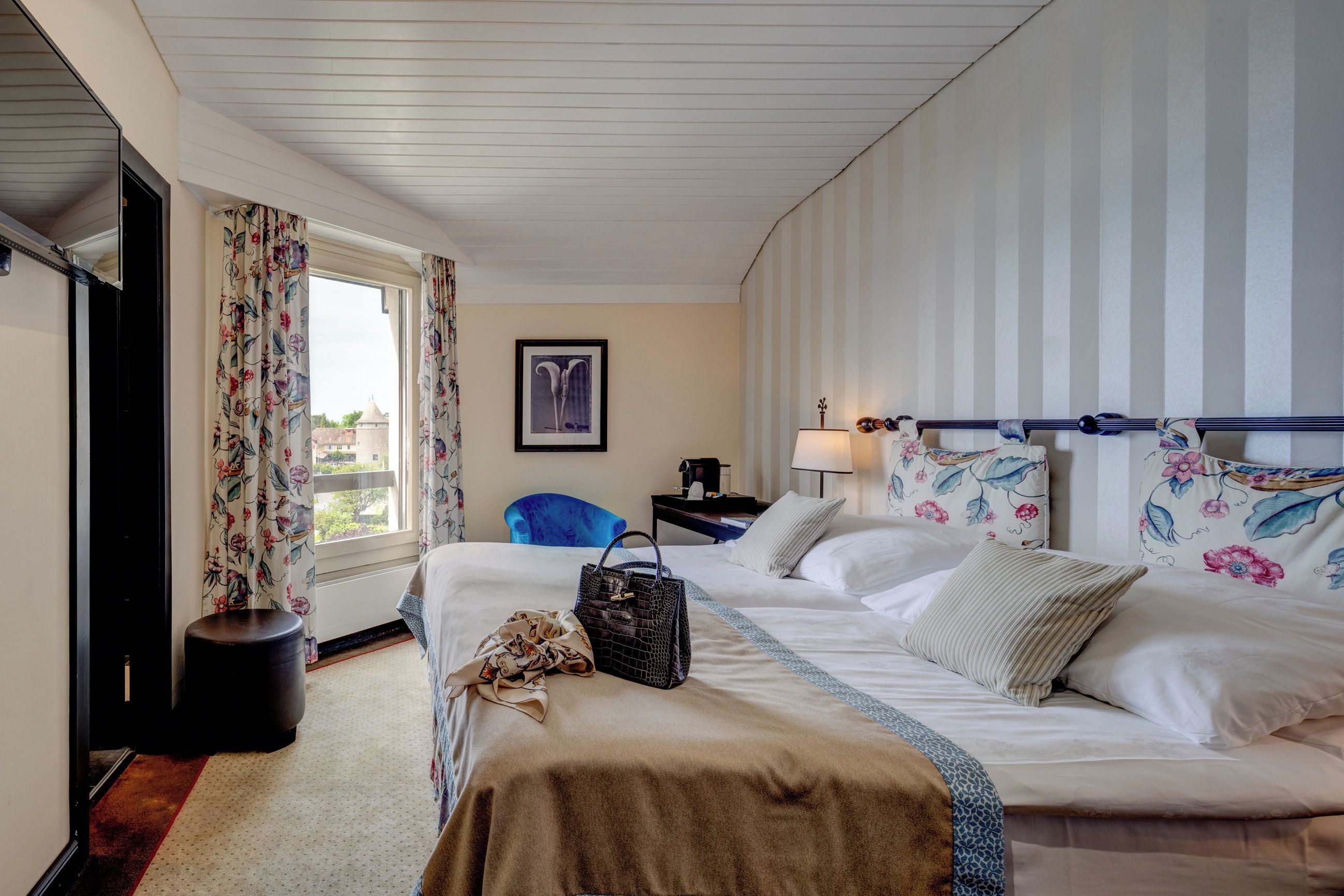 A hotel room with a large bed, a chair, a desk, and a window with curtains.