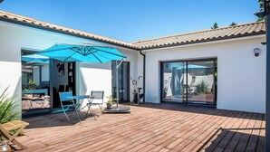Une terrasse moderne avec une plateforme en bois, un parasol bleu et une porte vitrée donnant sur un espace intérieur.