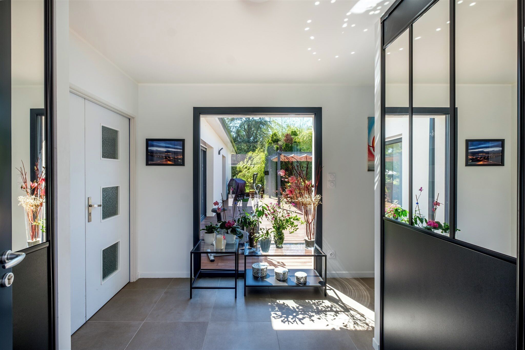 A hallway with a glass door leading to a patio area with potted plants and outdoor seating.