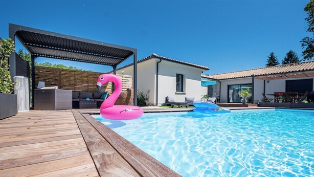 Une piscine avec une terrasse en bois, un flotteur en forme de flamant rose et un patio couvert.