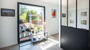 Un intérieur moderne avec une grande porte vitrée donnant sur un espace extérieur, une œuvre d’art minimaliste encadrée de noir accrochée au mur, et une table basse en verre agrémentée d’objets décoratifs.