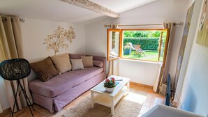 Ein Wohnzimmer mit Sofa, Couchtisch und Blick auf einen Garten durch ein offenes Fenster.