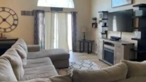 Een woonkamer met een hoekbank, een flatscreen televisie en een grote klok aan de muur.