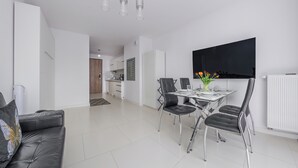 A modern living room with a dining area, a kitchen in the background, and a flat-screen TV mounted on the wall. - Apartamenty Sun & Snow Na Wydmach (Dziwnów)
