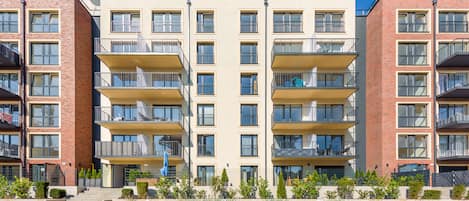 Un immeuble résidentiel à plusieurs étages, doté de balcons, d’une entrée principale et d’un jardin paysager à l’avant.