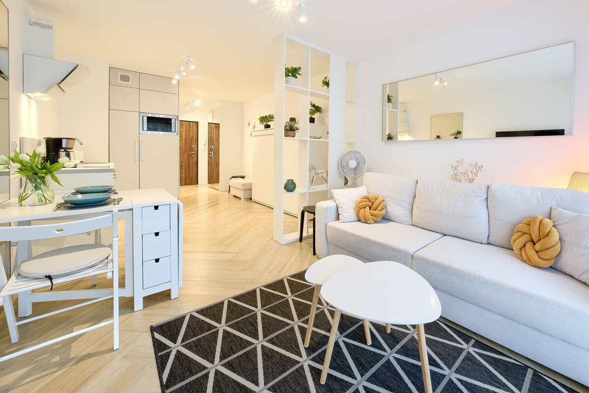 Un salon moderne avec un canapé blanc, une petite table blanche, un tapis noir et blanc et un bureau blanc avec des tiroirs.