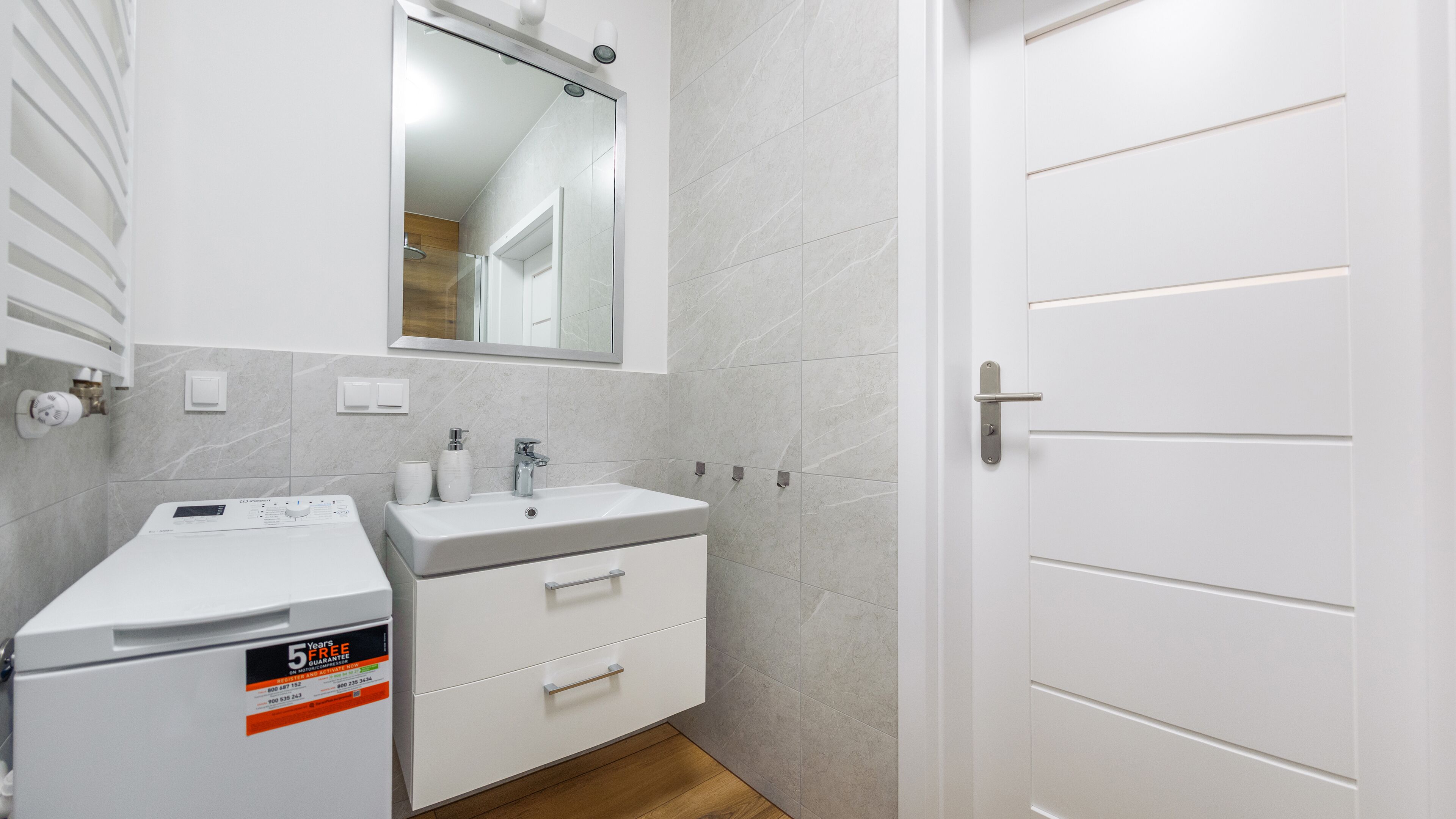 A bathroom with a white sink, mirror, and a white toilet. There is a white cabinet with drawers and a white door.