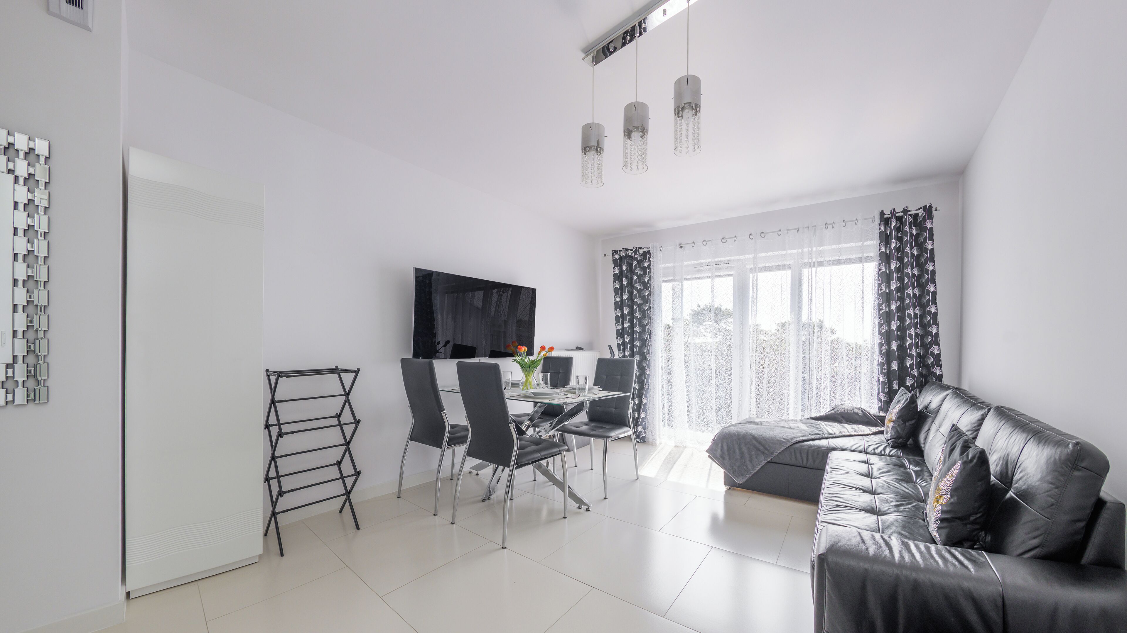 Een moderne woonkamer met een eethoek, een zwarte leren bank, een aan de muur bevestigde televisie en een raam met behang.