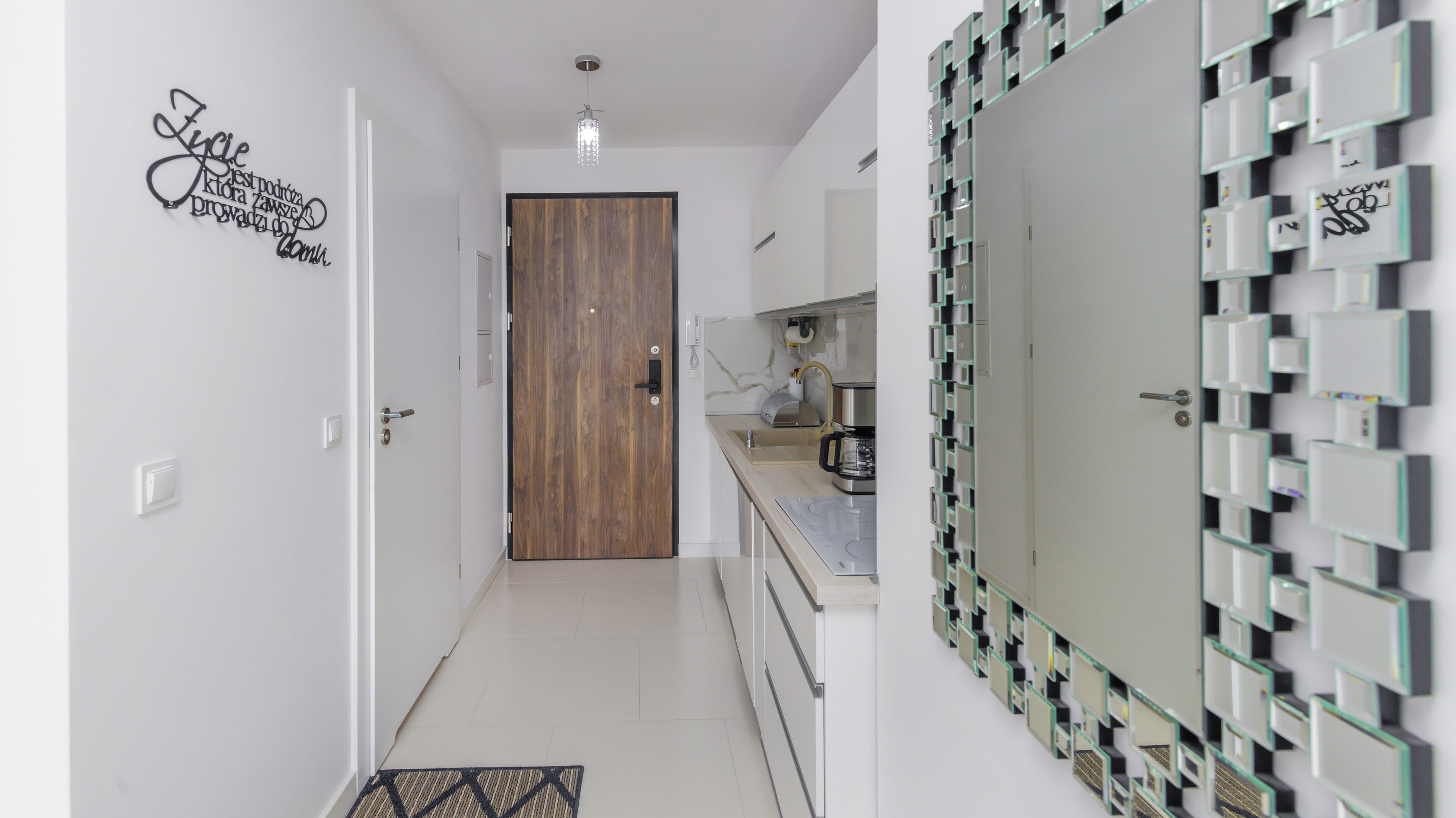 A modern kitchen with a wooden door, a built-in stove, and a wall-mounted mirror with a geometric pattern.