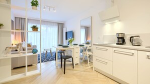 A modern, well-lit hotel room with a dining area, kitchenette, and a seating area with a sofa and a small table. - Apartamenty Sun & Snow Na Wydmach (Dziwnów)