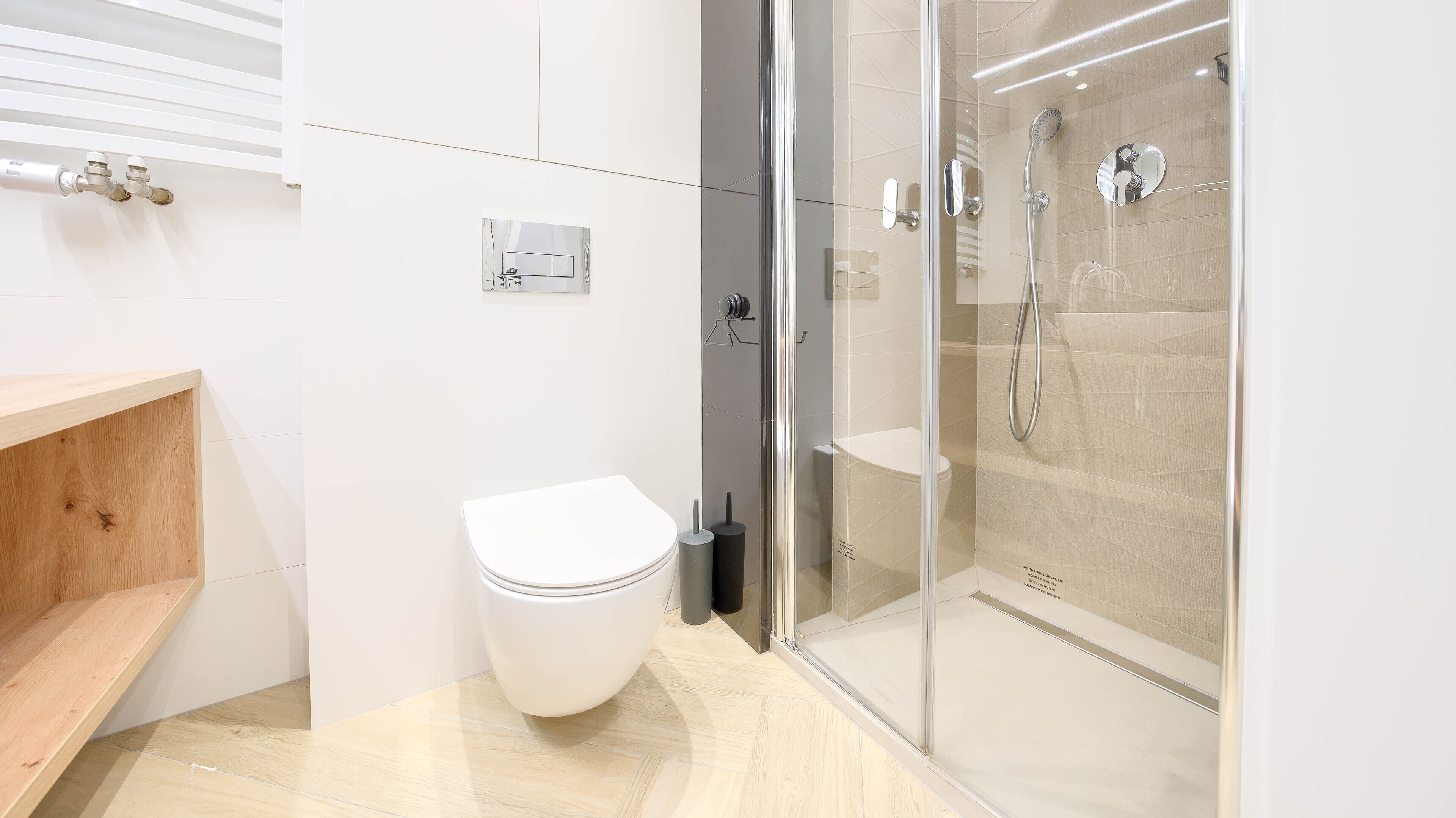A modern bathroom with a toilet, a glass shower enclosure, and a wooden shelf.