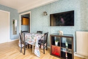 A dining area with a table set for four, a flat-screen TV mounted on the wall, and a small cabinet with decorative items.