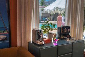 A room with a coffee machine, a potted plant, and a small table with books and a card holder. - Blush & Beachy · Colorful King Coastal Suite (Clearwater)