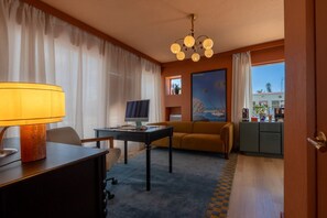 A hotel room with a desk, a sofa, a television, a painting, and a view of the outside.