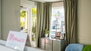 A hotel room with a view of palm trees and a balcony. There is a desk with a coffee maker and a plant. Two chairs are visible, one blue and one green. - 101 · ☀Pool✔ Beach✔ Self Checkin✔ Free Parking✔ (Clearwater)