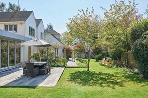 A patio with outdoor furniture, a covered table, and a view of a house with a garden. - The Chase (Cheltenham)
